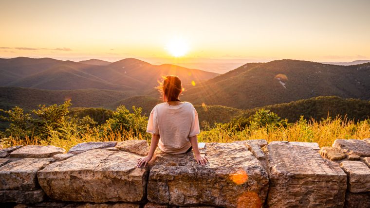 View of woman sees sunset over blue ridge mountains from skyline