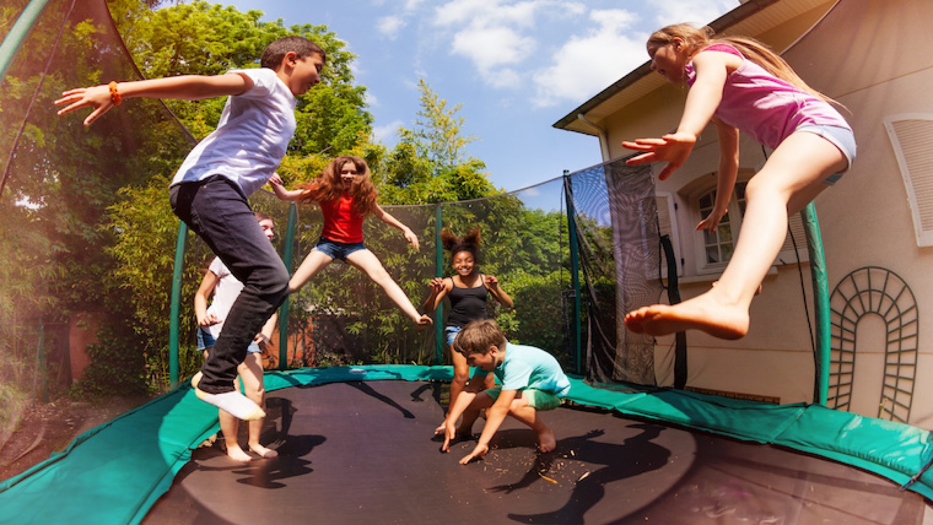 Portrait of happy friends, multiethnic boys and girls, jumping on the backyard trampoline in summer
